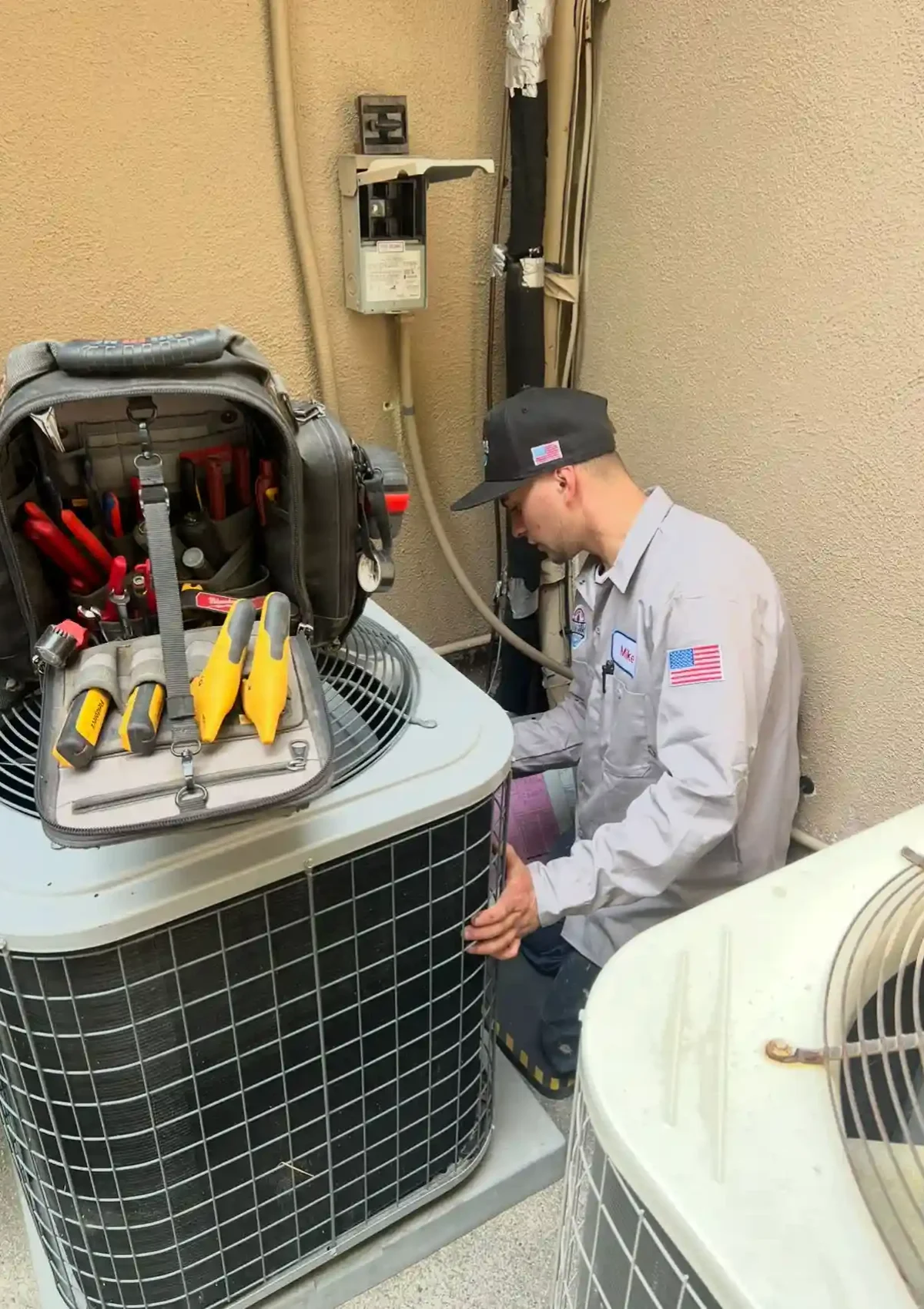 Male HVAC contractor on his knees works on a single air conditioning unit, his tools in front of him.